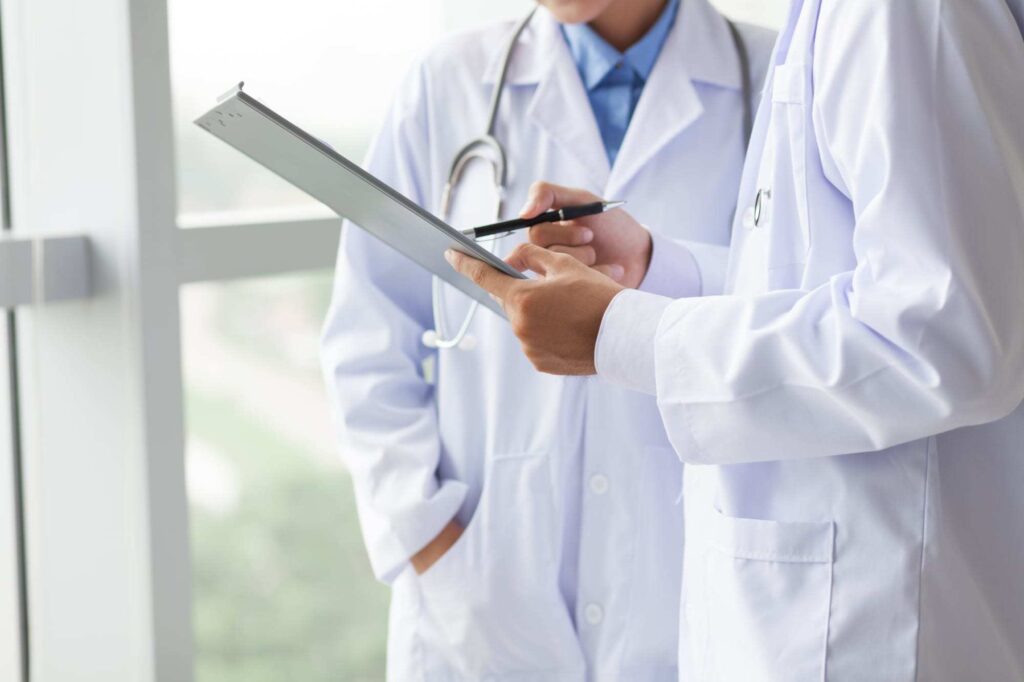 Close-up of torsos of two doctors sharing notes.
