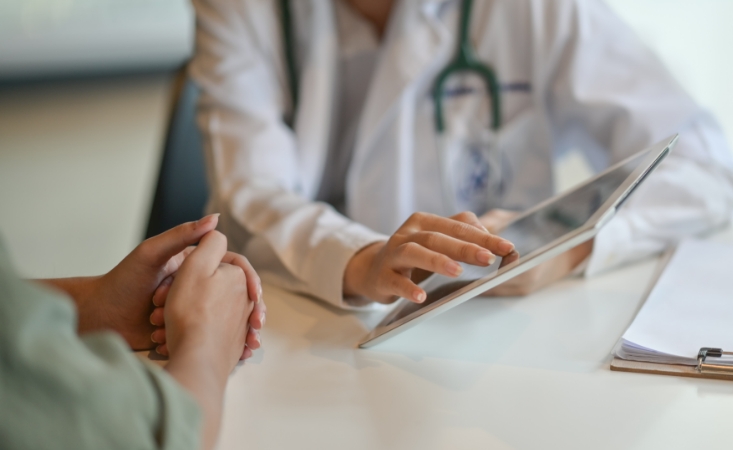 A doctor holding a tablet while consulting with a patient.