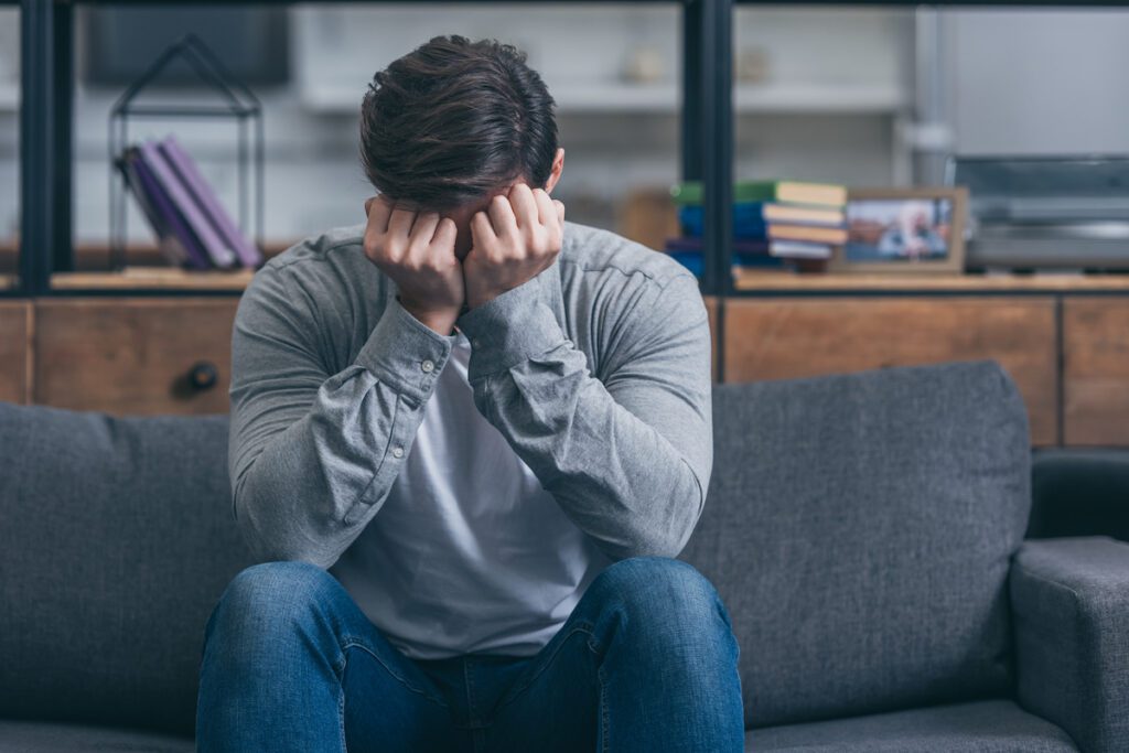 man sitting on couch, crying and and covering face with hands at home image