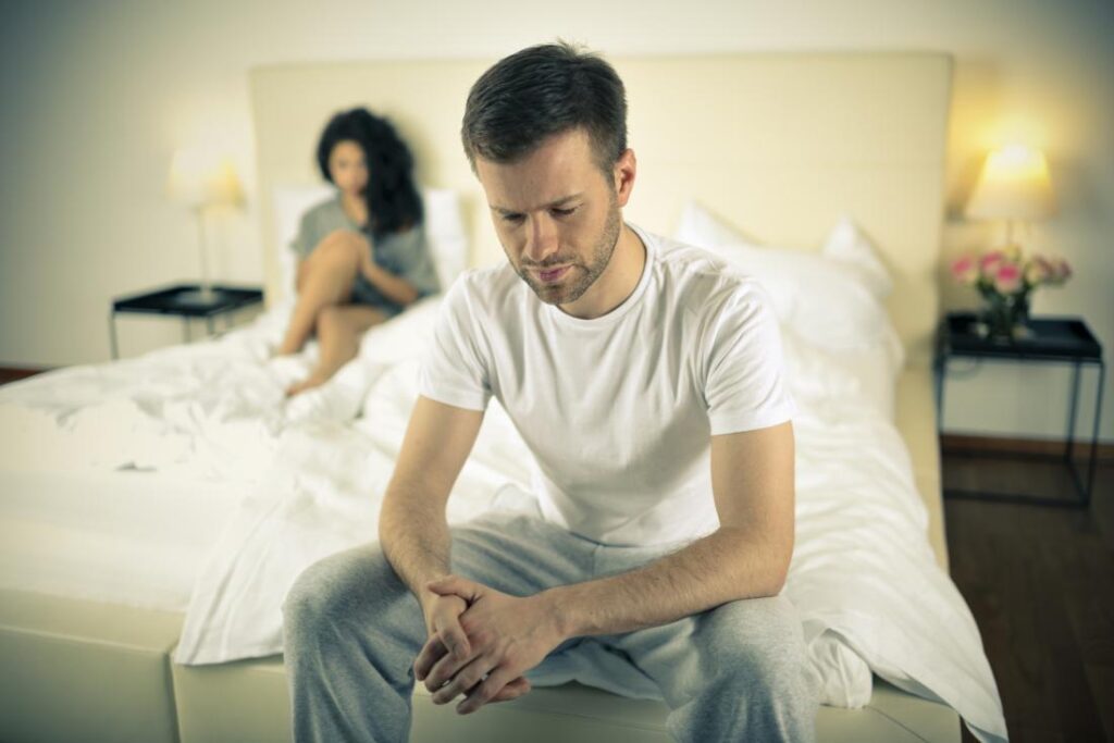 An anxious man sitting on the end of his bed, contemplating erectile dysfunction reversal.