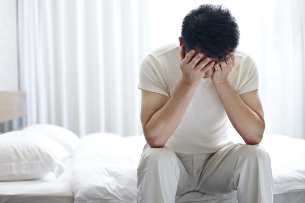 An anxious man sitting on the edge of his bed.
