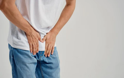 Man holding his groin in pain, wearing jeans and a t-shirt